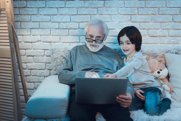 Grandfather and grandson sitting on couch and watching movie on laptop - Valokuva, kuva