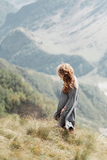 Menina bonita nova em um vestido longo está de pé junto ao penhasco no fundo das montanhas
 - Foto, Imagem