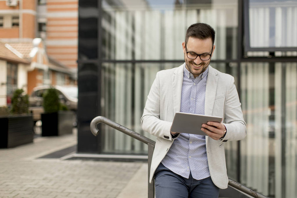schöner junger Geschäftsmann mit digitalem Tablet am Bürogebäude - Foto, Bild