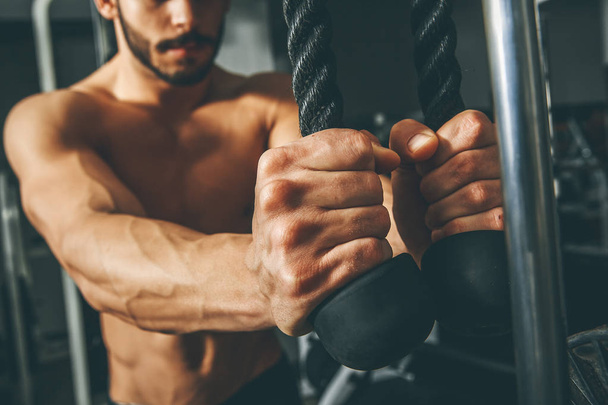 nackter Oberkörper muskulöser Mann trainiert im Fitnessstudio und macht Übungen mit Trizeps-Seil - Foto, Bild