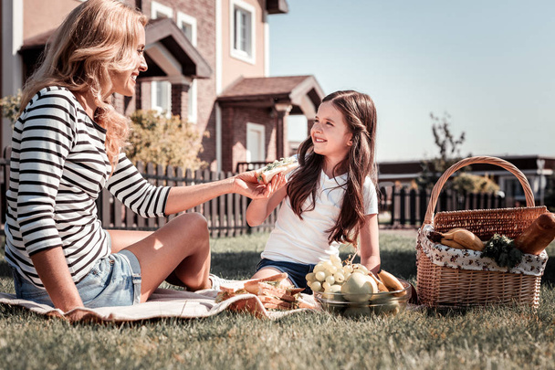 Caring cute mother sitting and giving a sandwich. - 写真・画像