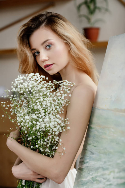 mooi mals meisje houdt van witte bloemen en camera van kunststudio te kijken   - Foto, afbeelding