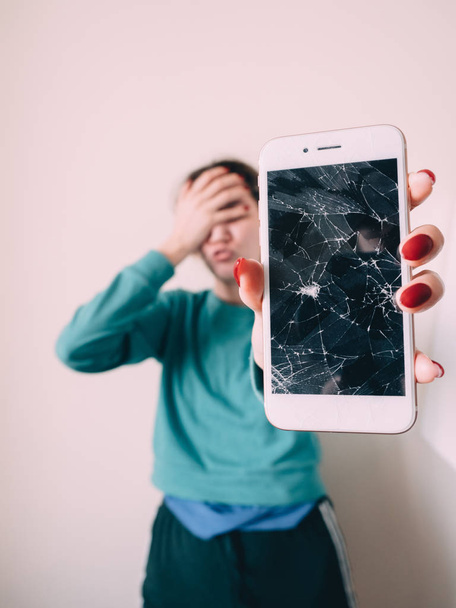 Broken glass screen smartphone in hand of upset girl, white background - Fotó, kép
