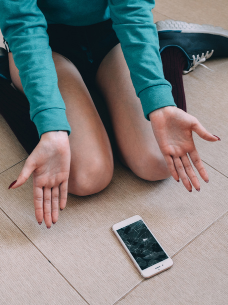 Girl with broken screen smartphone on the tile floor  - Foto, Bild