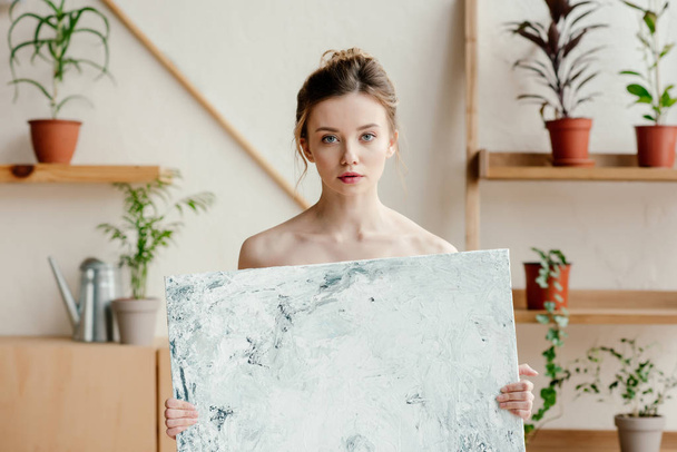 beautiful young naked artist holding picture and looking at camera - Foto, immagini