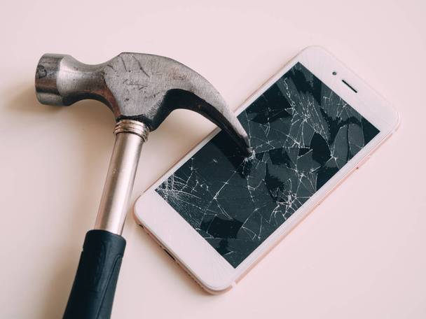 gebroken scherm van de smartphone met hamer op witte tafel - Foto, afbeelding