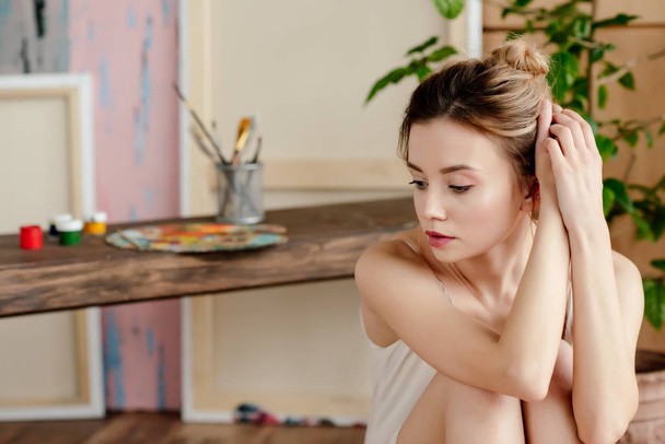 beautiful pensive young woman sitting and looking away in art studio - Foto, afbeelding