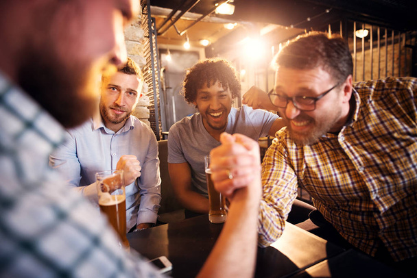 jeunes hommes barbus heureux boire avec de la bière dans un pub et avoir défi bras de fer
  - Photo, image