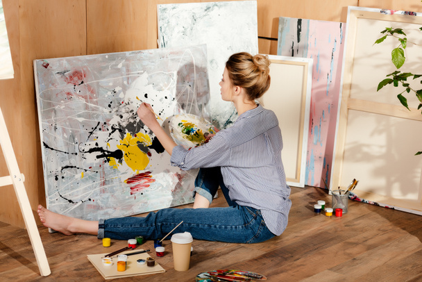 hermosa joven pintora sentada en el suelo y dibujo de la imagen en el estudio de arte
 - Foto, Imagen