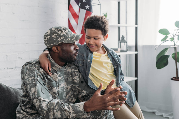 Afro-Amerikaanse jongen knuffelen en luisteren naar zijn vader in het leger uniform - Foto, afbeelding
