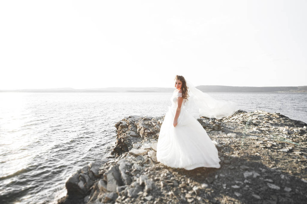 Pretty lady, bride posing in a wedding dress near sea on sunset - Fotó, kép