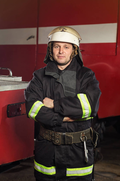 Brandweerman (brandweerman) in actie staande in de buurt van een brandweerwagen. Emer - Foto, afbeelding