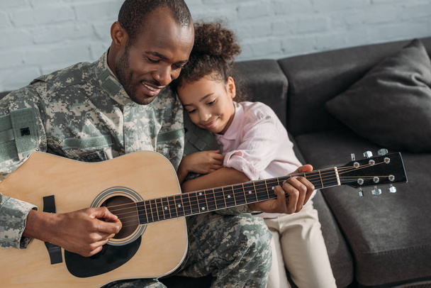  Χαμογελαστός στρατιώτης παίζοντας κιθάρα και αγκαλιάζει κόρη - Φωτογραφία, εικόνα