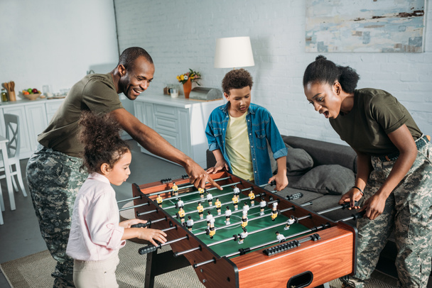 Woman and man in army uniform and cheerful kids playing table football  - Fotó, kép