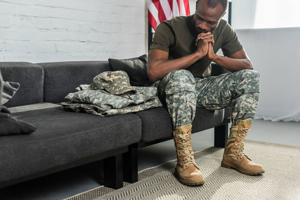 Thoughtful soldier sitting on sofa and looking at his camouflage clothes - Foto, Imagem