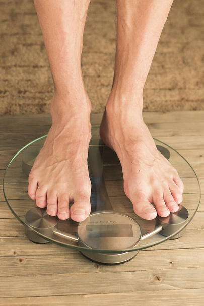 Man stands on the scales. Male feet on glass scales and wooden floor - Photo, Image