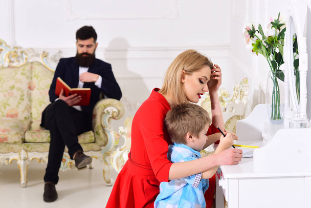 Home schooling concept. Father reading book, while mother teaches son preschooler to draw or write, luxury interior. Kid growthing in welfare. Parents enjoying parenthood, happy. - Фото, зображення