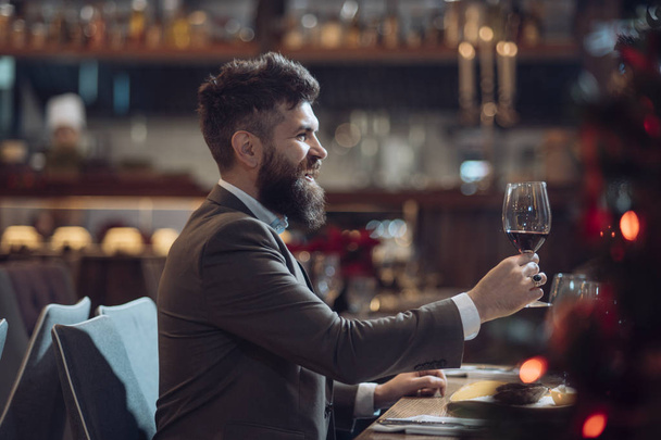 Portrait of handsome young man smiling and holding glass of red wine over blurry background - Foto, Imagem