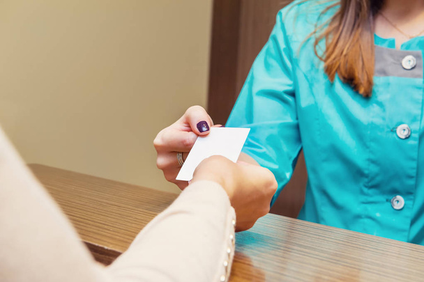 Close up of receptionist give visit card with empty blank to female patient in medical clinic. Selective focus, space for text. - Photo, image