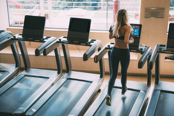 femme courant sur des tapis roulants dans une salle de gym avec une belle lumière des machines de gymnastique de fenêtre
 - Photo, image
