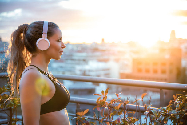 αθλήτρια σε εξωτερικούς χώρους στο γυμναστήριο ηρεμίας απολαμβάνοντας την πόλη προβολές ακούγοντας μουσική - Φωτογραφία, εικόνα