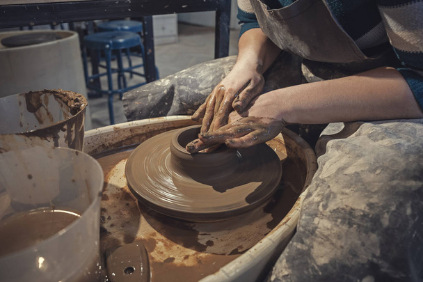 Craftsman woman potter in apron at work. Craftsman artist shapes the jug with his hands on pottery wheel - Фото, зображення