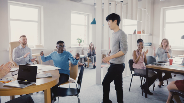 Câmera segue feliz asiático homem fazendo engraçado vitória celebração dança andar no escritório, colegas bater palmas e rir 4K
. - Filmagem, Vídeo