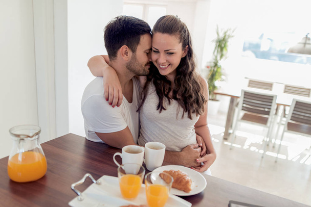 Młoda szczęśliwa para siedzi w nowoczesnym mieszkaniu i je razem śniadanie. - Zdjęcie, obraz