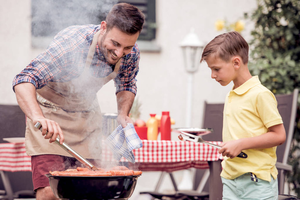 Man cooking meat on barbecue grill with son - Photo, Image