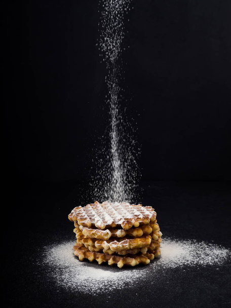 White plate with homemade Belgian waffles, on top of poured sifting of powdered sugar on black background, very tasty snack. sugar over old wooden table. Dark rustic style. copy space, stylish - Фото, изображение