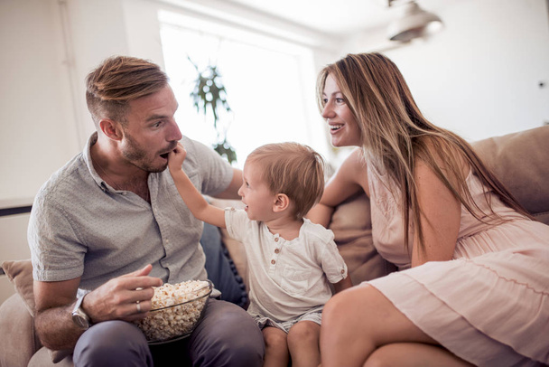 Happy father, mother and son relaxing at home and eating popcorn - Photo, Image