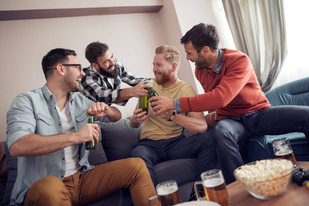 Χαμογελώντας αρσενικούς φίλους πίνοντας μπύρα στο σπίτι. - Φωτογραφία, εικόνα