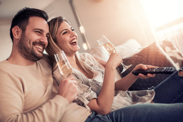 glückliches junges Paar entspannt sich zu Hause, schaut Film und trinkt Wein. - Foto, Bild