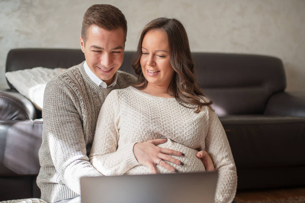 Pregnant woman wathing video on laptop with husband at home. - Photo, image