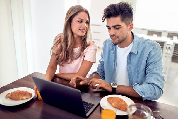 Young cute couple having breakfast while browsing laptop. - Foto, afbeelding
