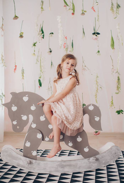 Ładna dziewczynka w sukni z zabawek koń w domu, szczęśliwe dzieciństwo koncepcja  - Zdjęcie, obraz