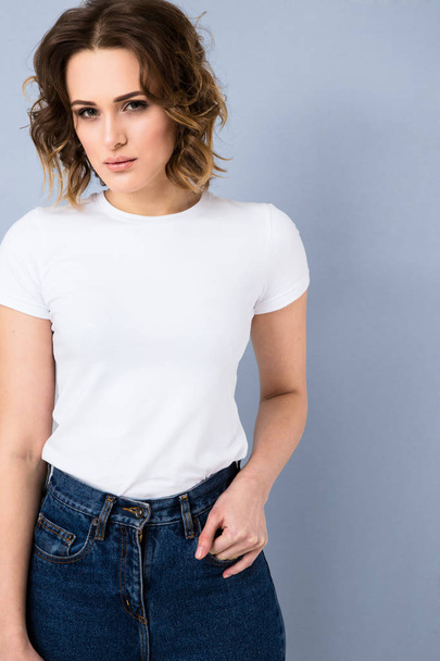 Portrait of stylish young girl in basic white t-shirt and high waisted blue jeans  posing in studio on grey background - Foto, Imagem