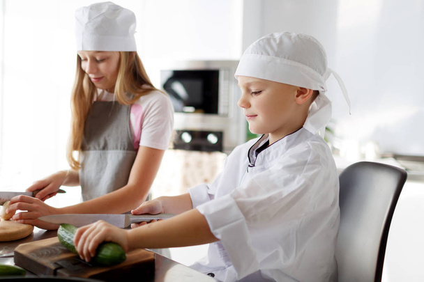A brother and a sister cutting  vegetables  in the modern kitchen room. Happy family cooking concept. - Фото, изображение