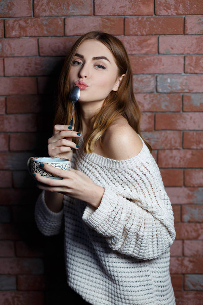 Young beautiful woman drinking a cup of coffee in the cafe on a red brick wall background. Stylish lady with hot drink. - Foto, Imagen