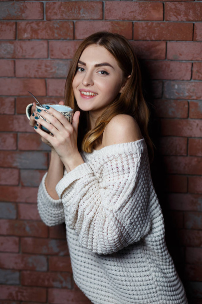 Young beautiful woman drinking a cup of coffee in the cafe on a red brick wall background. Stylish lady with hot drink. - Photo, Image