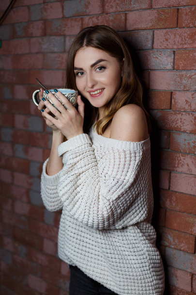 Young beautiful woman drinking a cup of coffee in the cafe on a red brick wall background. Stylish lady with hot drink. - Foto, afbeelding