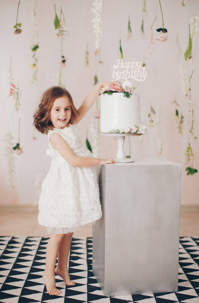niedliches kleines Mädchen im Kleid mit Kuchen zu Hause, glückliche Kindheit Konzept  - Foto, Bild