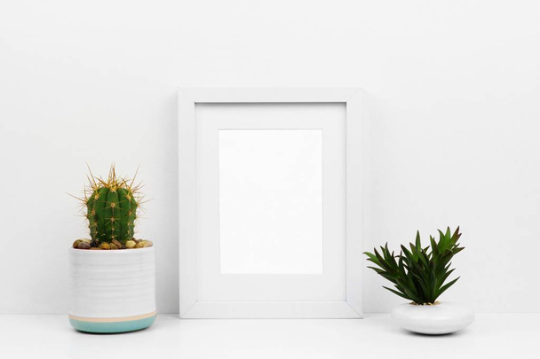 Simular marco blanco con cactus y suculenta en un estante o escritorio. Esquema de color blanco. Orientación del marco retrato
. - Foto, Imagen