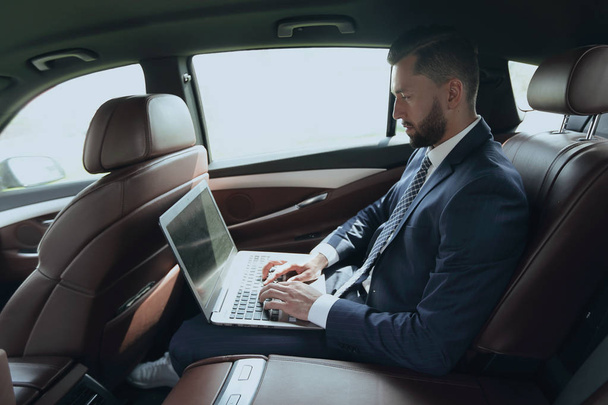 businessman using a laptop in the backseat of a car - Foto, afbeelding