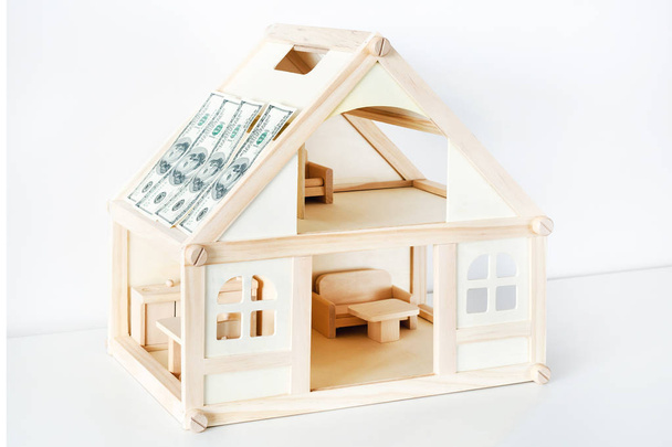 Dřevěný dům model. Střecha budovy je pokrytá dolarové bankovky. Pojem pojištění nemovitosti - Fotografie, Obrázek