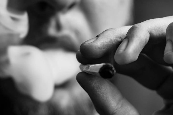 joint in man hand. A man smokes cannabis weed, a . Smoke on a black background. Concepts of medical marijuana use and legalization of the cannabis.Black and white - Fotografie, Obrázek