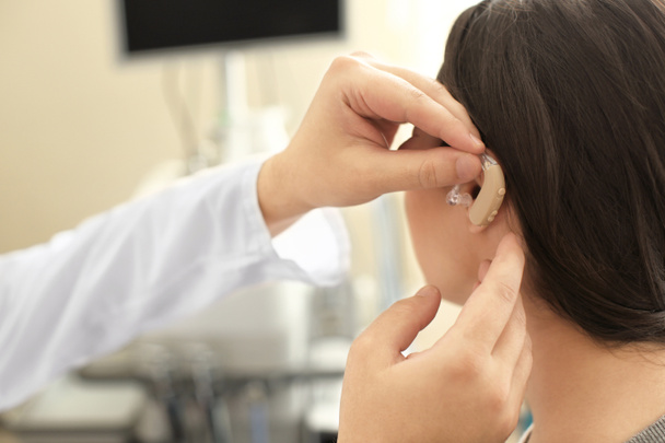 Отоларинголог помещает слуховой аппарат женщине в ухо
 - Фото, изображение