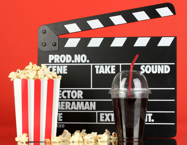 Movie clapperboard, cola and popcorn on red background - Photo, image