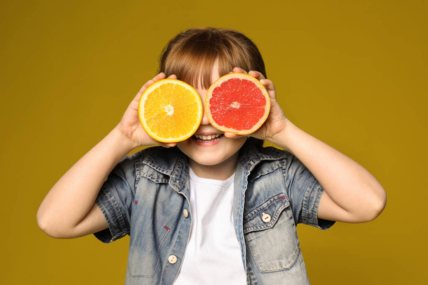 niedliches kleines Mädchen mit Zitrusfrüchten auf farbigem Hintergrund - Foto, Bild