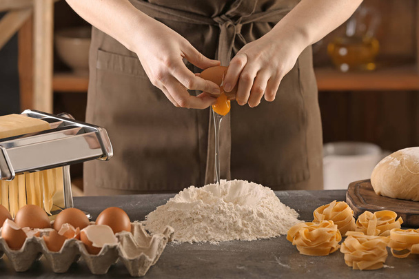 Woman breaking egg into flour at table. Pasta recipe - Foto, afbeelding